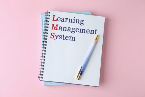Notebook with text Learning Management System and red initial letters forming initialism LMS on pink background, top view